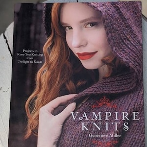 May include: A book cover featuring a woman with red hair and red lipstick wearing a purple knitted hood. The book title is "Vampire Knits" by Genevieve Miller. The cover also includes the text "Projects to Keep You Knitting from Twilight to Dawn."