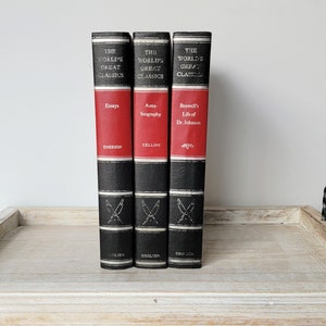 May include: Three hardcover books with black spines and red accents. The books are part of "The World's Great Classics" series and feature the titles "Essays" by Emerson, "Autobiography" by Cellini, and "Boswell's Life of Dr. Johnson".