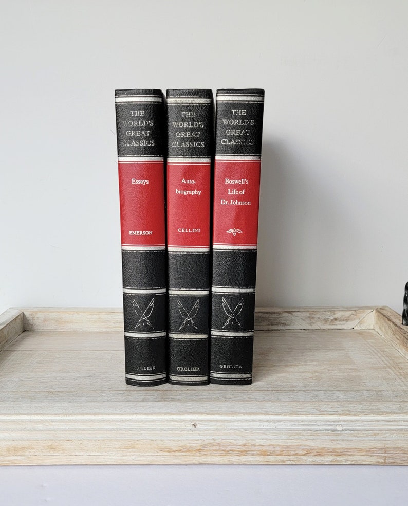 May include: Three hardcover books with black spines and red accents. The books are part of "The World's Great Classics" series and feature the titles "Essays" by Emerson, "Autobiography" by Cellini, and "Boswell's Life of Dr. Johnson".