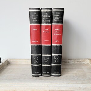 May include: Three black and red hardcover books with gold lettering. The books are part of a series called "The World's Great Classics". The titles are "Essays" by Emerson, "Auto-biography" by Cellini, and "Boswell's Life of Dr. Johnson".