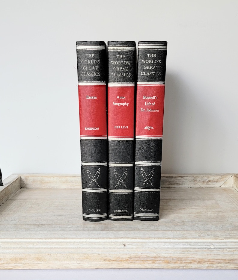 May include: Three black and red hardcover books with gold lettering. The books are part of a series called "The World's Great Classics". The titles are "Essays" by Emerson, "Auto-biography" by Cellini, and "Boswell's Life of Dr. Johnson".