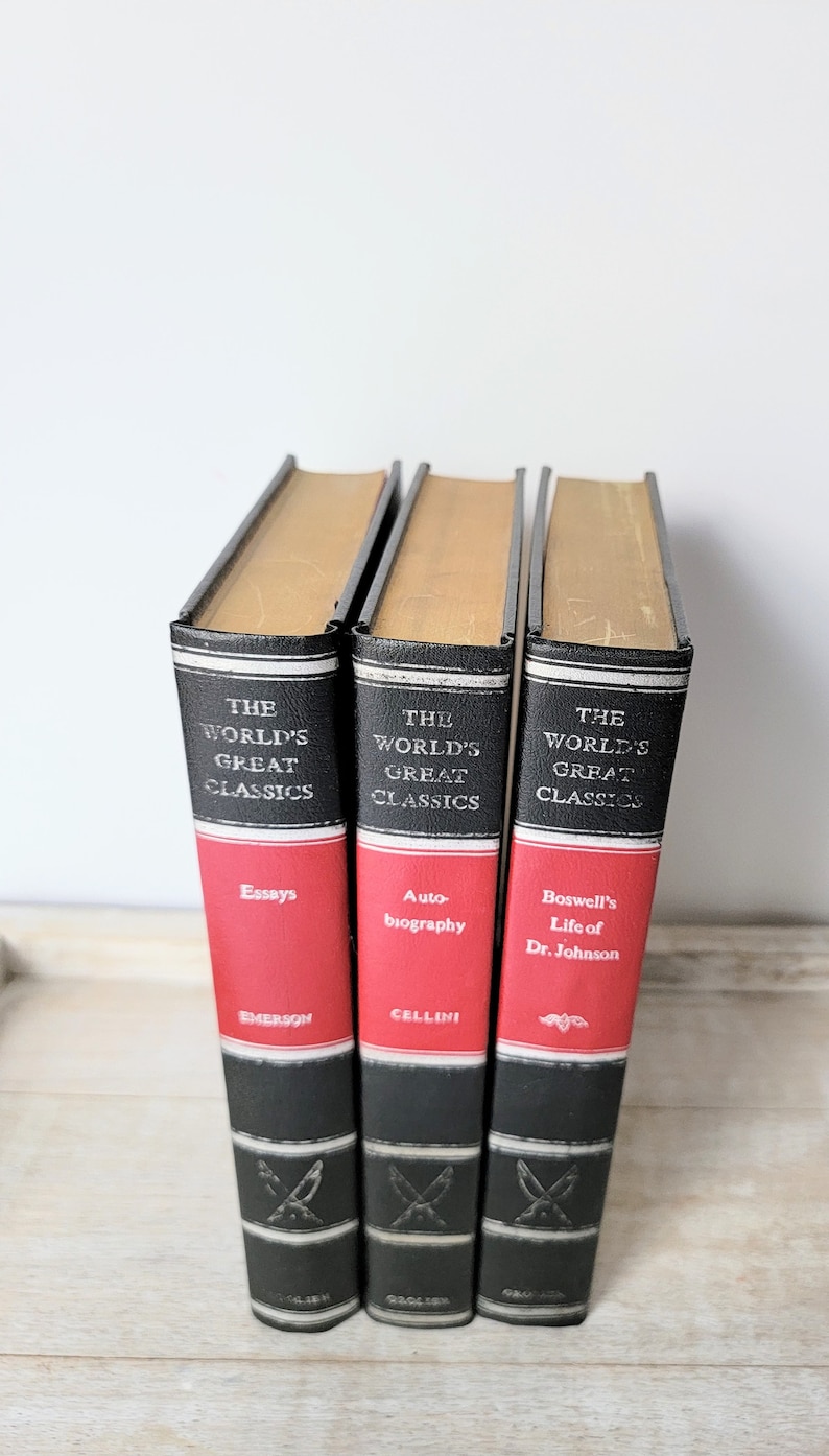 May include: Three hardcover books with black spines and red covers. The books are part of a series called "The World's Great Classics". The titles are "Essays" by Emerson, "Auto-biography" by Cellini, and "Boswell's Life of Dr. Johnson".