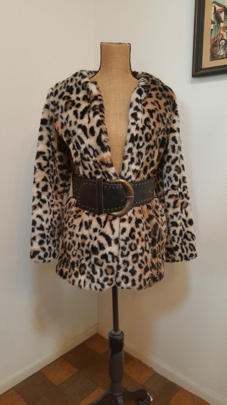 May include: A brown, black, and white leopard print faux fur jacket with a brown leather belt with a large silver buckle.
