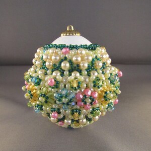 以下が含まれることがあります： 白いクリスマスオーナメントは、白いパール、緑、ピンク、黄色のビーズなど、さまざまなビーズで覆われています。