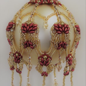 May include: A gold and burgundy beaded Christmas ornament with a teardrop shape and dangling beads.