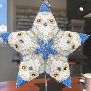 May include: A white and blue beaded star ornament with a snowflake design in the center. The star is decorated with images of owls.