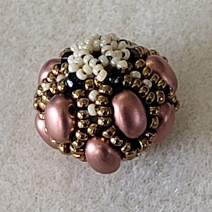 May include: A small, round bead made of various beads in shades of gold, white, black, and rose gold. The bead is a mix of small round beads and larger oval beads.