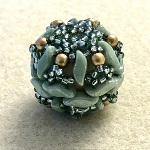 May include: A round bead with a green and gold design. The bead is made of small, faceted beads and larger, flat beads. The bead is a light green color with gold accents.