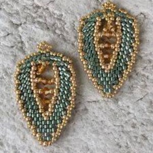 Pode incluir: Dois brincos em forma de folha feitos de contas. Cada brinco apresenta um contorno de contas douradas e um design central em ouro e verde. Os brincos são exibidos em uma superfície texturizada cinza claro.