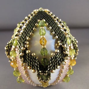 以下が含まれることがあります： 金色、緑色、茶色のビーズで幾何学模様が施された、白い卵型のオーナメント。オーナメントは繊細で複雑なデザインです。