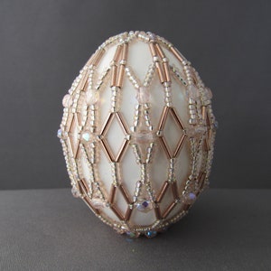 May include: A white egg decorated with a geometric pattern of gold and iridescent beads.