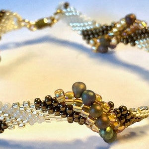 Könnte beinhalten: Ein Armband mit Perlen in Spiralform. Das Armband besteht aus braunen, weißen und goldenen Perlen.