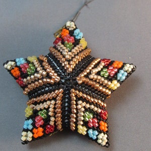 May include: A beaded star ornament with a five-point design. The star is primarily black with intricate patterns in copper, white, and colorful beads. Small clusters of red, orange, blue, and green beads are scattered across the star's surface. A gray string is attached for hanging.