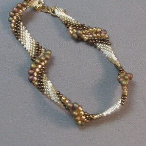 Op de afbeelding: Een bruin, wit en gouden kralen armband met een gedraaid ontwerp.