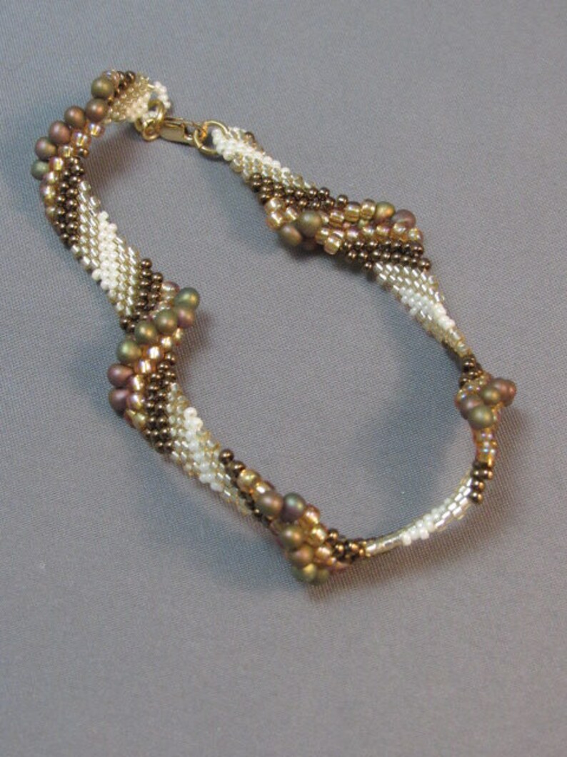 Op de afbeelding: Een bruin, wit en gouden kralen armband met een gedraaid ontwerp.
