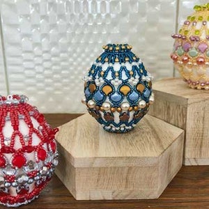 May include: Three beaded Easter eggs, each with a different color scheme and design. The eggs are displayed on wooden stands.