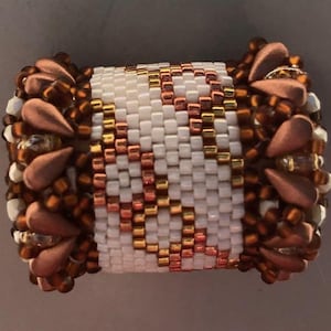 May include: A beaded bracelet featuring a baseball design. The bracelet has a white center with a baseball pattern in copper and gold beads. The edges are adorned with copper-colored teardrop-shaped beads and smaller brown beads.