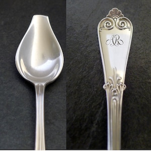 May include: A silver spoon with an ornate handle and a rounded, teardrop-shaped bowl. The handle is engraved with the initials "AR".