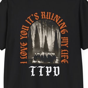 Könnte beinhalten: Schwarzes T-Shirt mit einem orangefarbenen Grafikdruck einer Waldszene mit dem Text "I love you it's ruining my life" und "TTPD" unter dem Bild.