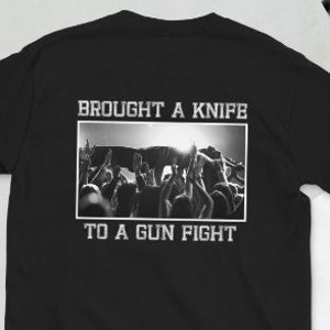 Könnte beinhalten: Schwarzes T-Shirt mit dem Text "BROUGHT A KNIFE TO A GUN FIGHT" über und unter einem Schwarz-Weiß-Bild einer Menge mit erhobenen Armen. Das Shirt hat einen Rundhalsausschnitt und kurze Ärmel.