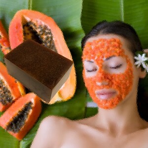 May include: A brown soap bar next to sliced papaya and a person with a papaya facial mask. The background is green. A white flower is in the person's hair. The image has a spa or wellness theme.
