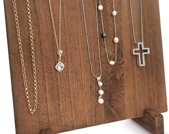 May include: A wooden jewelry display stand with a dark brown finish. Several necklaces of varying styles hang from the stand, including gold chains, a pendant necklace, and a pearl necklace. A cross pendant necklace is also displayed.