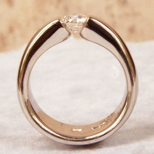May include: A simple silver band ring with a single, round, clear diamond set in the centre.