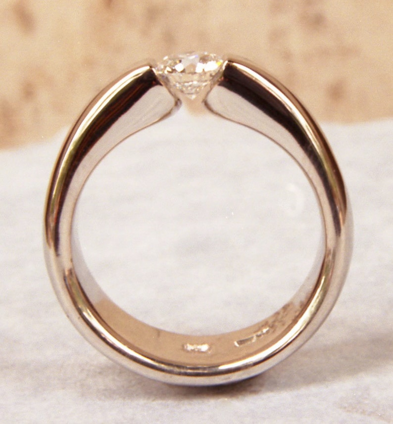 May include: A simple silver band ring with a single, round, clear diamond set in the centre.