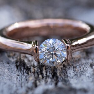 May include: A rose gold engagement ring with a single round brilliant cut diamond.