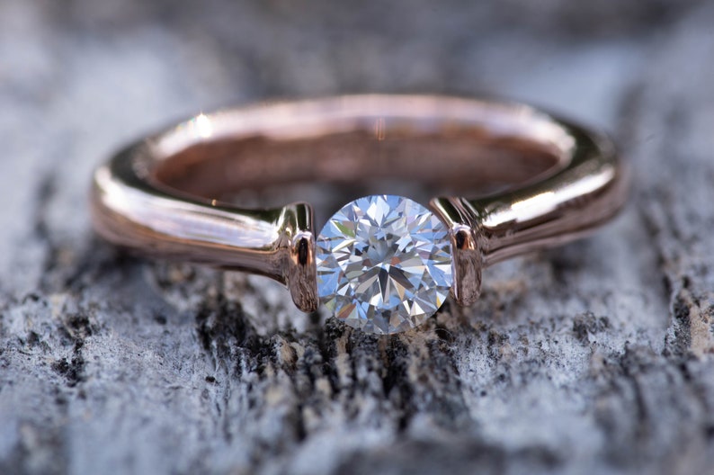 May include: A rose gold engagement ring with a single round brilliant cut diamond.