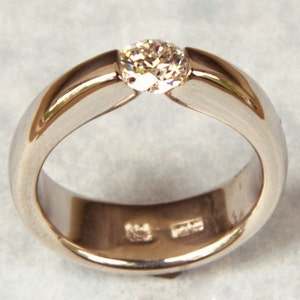 May include: A simple silver band ring with a single, round, clear diamond set in the centre.