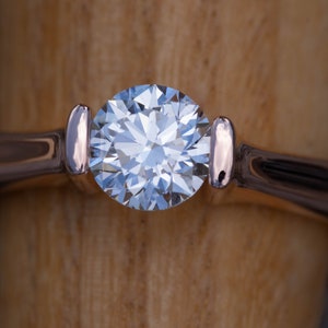 May include: A close-up of a solitaire engagement ring with a round brilliant cut diamond set in a rose gold band.