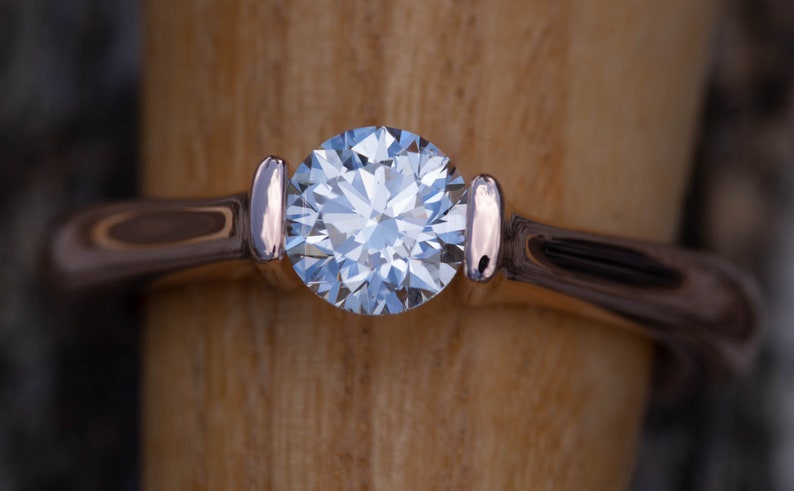 May include: A close-up of a solitaire engagement ring with a round brilliant cut diamond set in a rose gold band.