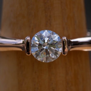 May include: A rose gold engagement ring with a round brilliant cut diamond.
