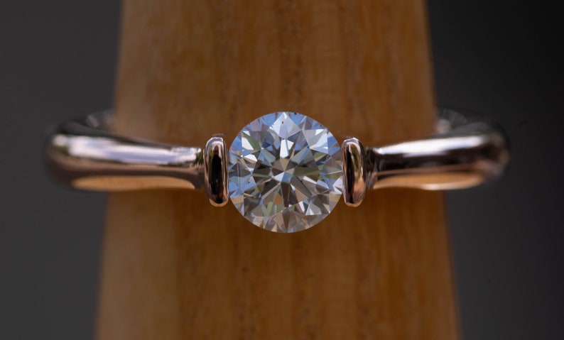 May include: A rose gold engagement ring with a round brilliant cut diamond.