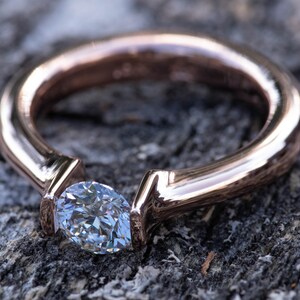 May include: A rose gold engagement ring with a single, clear, oval-shaped diamond set in a simple, modern design.