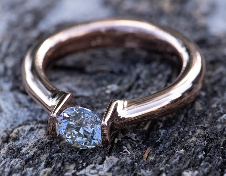 May include: A rose gold engagement ring with a single, clear, oval-shaped diamond set in a simple, modern design.