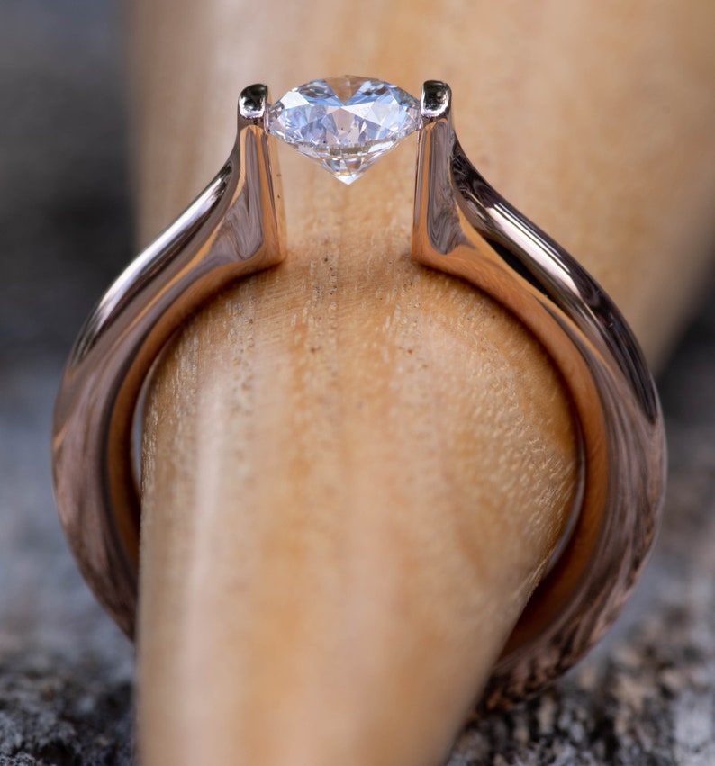 May include: A rose gold engagement ring with a single, clear, round diamond set in a bezel setting.