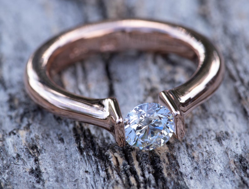 May include: A rose gold engagement ring with a single round diamond set in a unique prong setting.