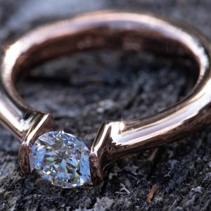 May include: A rose gold ring with a single, clear, pear-shaped diamond set in a simple, modern design.
