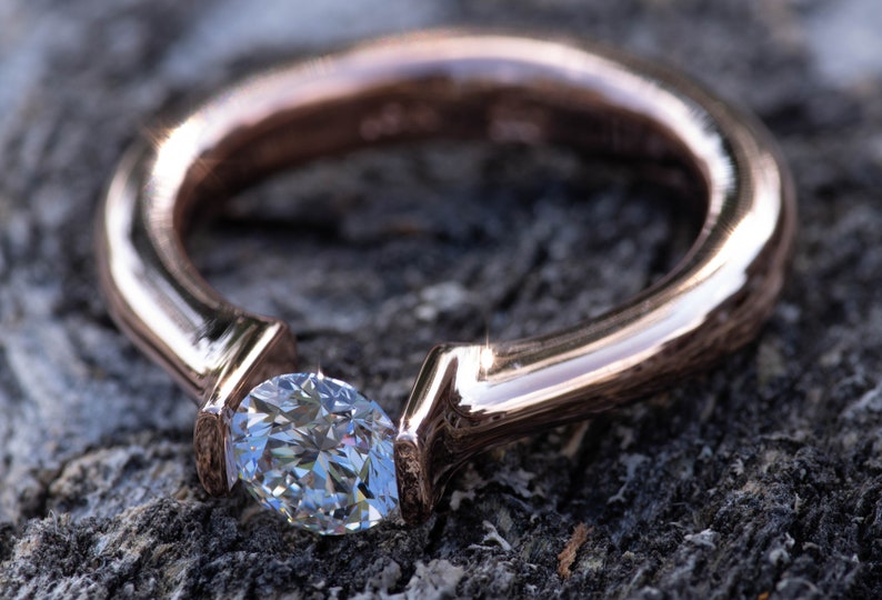 May include: A rose gold ring with a single, clear, pear-shaped diamond set in a simple, modern design.