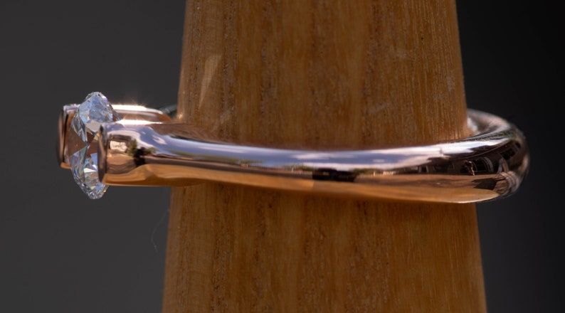 May include: A rose gold ring with a single, clear, round diamond set in a prong setting.