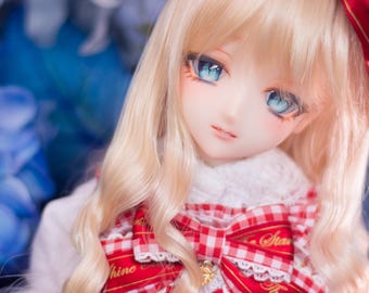 May include: A doll with long blonde hair, blue eyes, and a red and white checkered dress. She is wearing a red bow on her head and has a white collar.