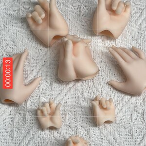 May include: A collection of articulated doll hands in various poses, made of a pale, flesh-toned material. The hands are arranged on a white, textured surface, with a timer overlay in the upper left corner.