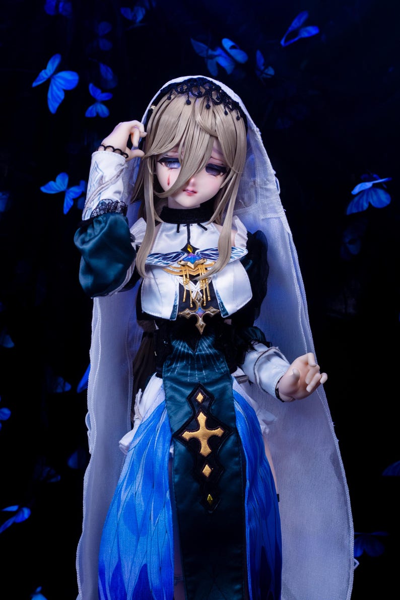 May include: A detailed doll with long blonde hair, wearing a white and blue dress with gold accents. The doll has a veil and is set against a dark background with blue butterfly accents. The doll's expression is somber.