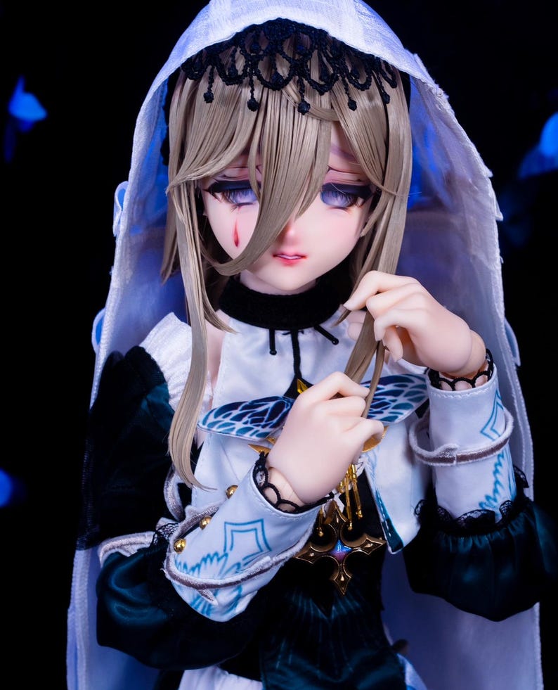 May include: A detailed doll with a pale complexion, wearing a white hooded veil with black lace trim. The doll has long, light brown hair and is dressed in a white and teal outfit with gold accents. A tear is visible on the doll's cheek.