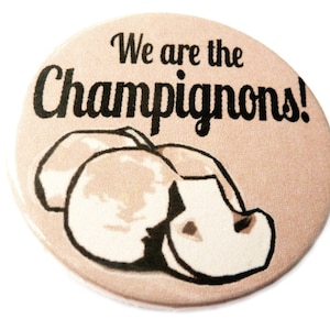 Könnte beinhalten: Ein runder Knopf mit hellbraunem Hintergrund. Der Knopf zeigt eine Schwarzweißillustration von Pilzen und den Text "We are the Champignons!"