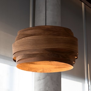 May include: A wooden pendant light fixture with a layered design. The light is on and emits a warm glow.