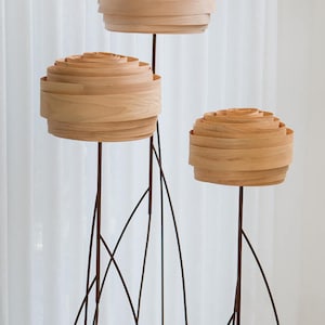 May include: Three wooden floor lamps with a unique design. The lamps have a round, layered shade made of wood and a thin black metal base.