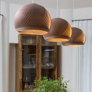 K&ouml;nnte beinhalten: Ein Esstisch aus Holz mit einer hellen Holzoptik. Drei braune, runde, geflochtene Pendelleuchten h&auml;ngen &uuml;ber dem Tisch. Eine Topfpflanze steht in der Mitte des Tisches.